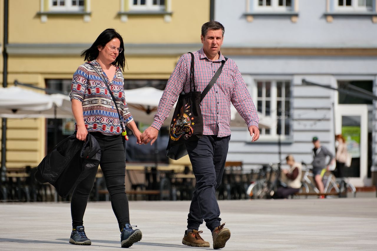 A casually dressed couple walks hand in hand in a bright urban setting, exuding warmth and connection.
