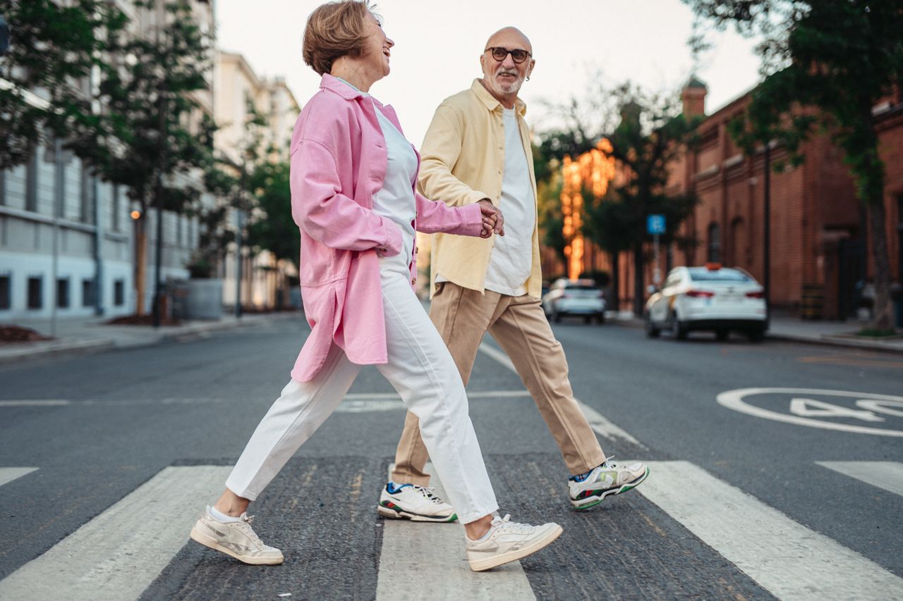 Happy senior couple holding hands and walking across a pedestrian crossing in an urban street.